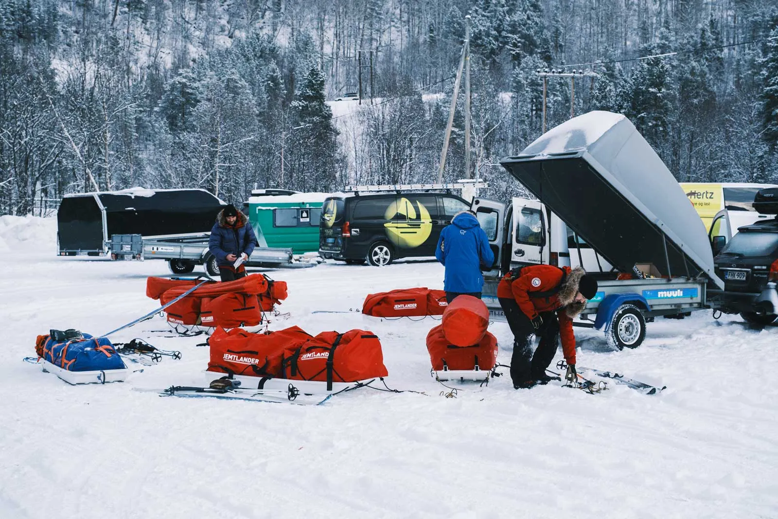 Ahkioita ja varusteita pakataan autojen vieressä lumisella parkkipaikalla