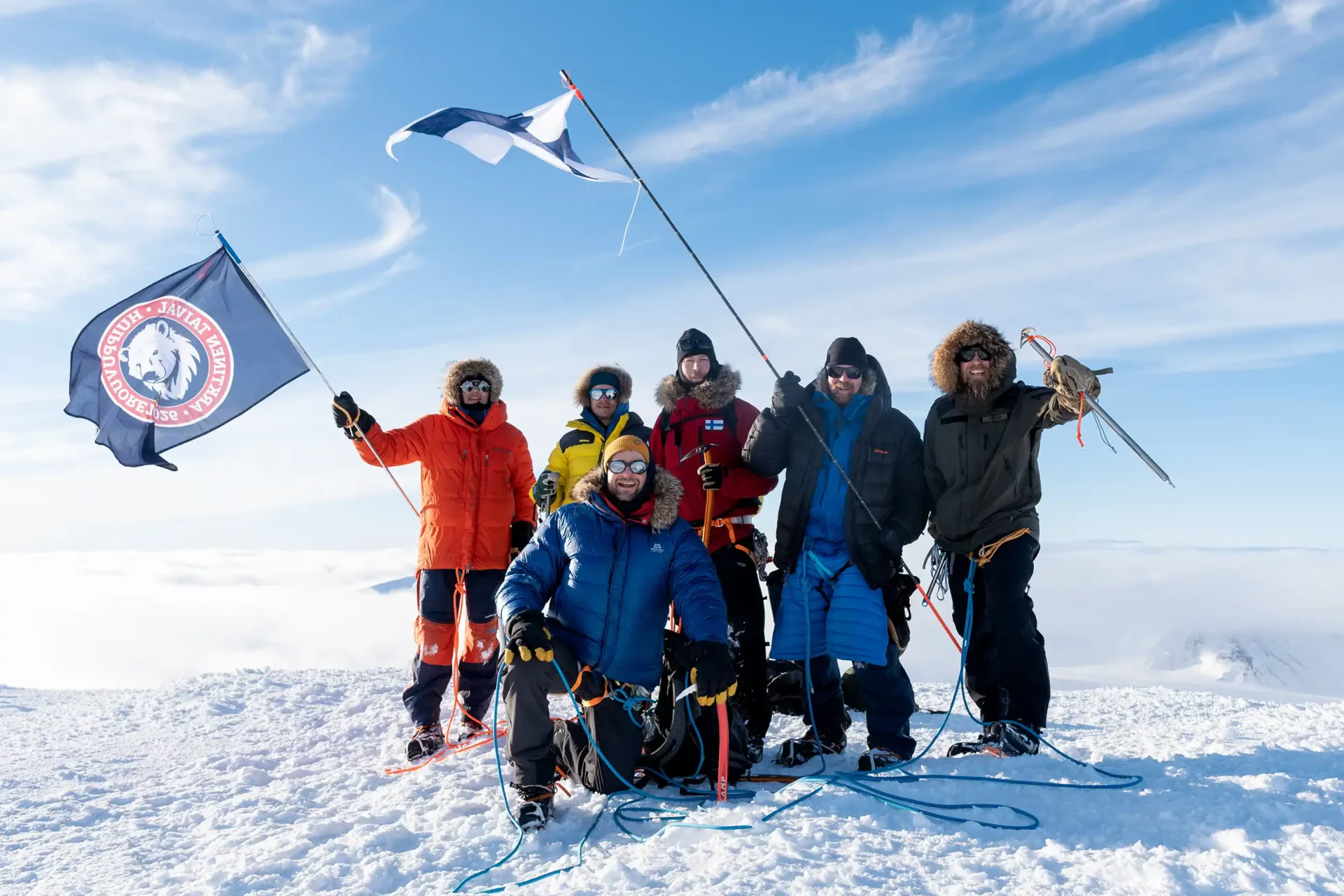 Retkikunta Newtontoppenin huipulla Suomen lipun ja retkikunnan lipun kanssa